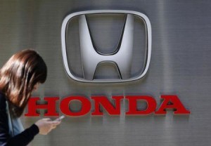 A woman using her mobile phone walks past a logo of Honda Motor Co outside the company's dealership in Tokyo October 28, 2014. REUTERS/Yuya Shino